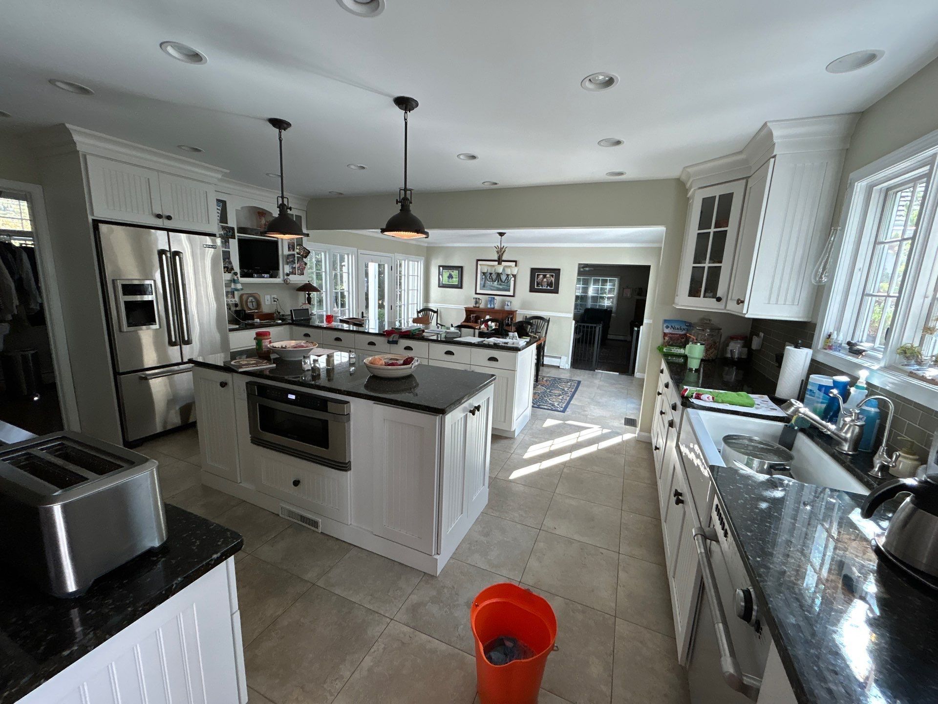 Spacious kitchen with white cabinets, black countertops, stainless steel appliances, and an orange bucket