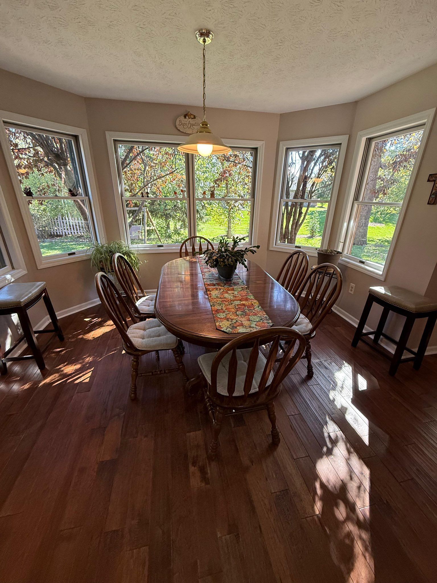 Dining room with a wooden table, chairs, and large windows. Sunlit hardwood floor