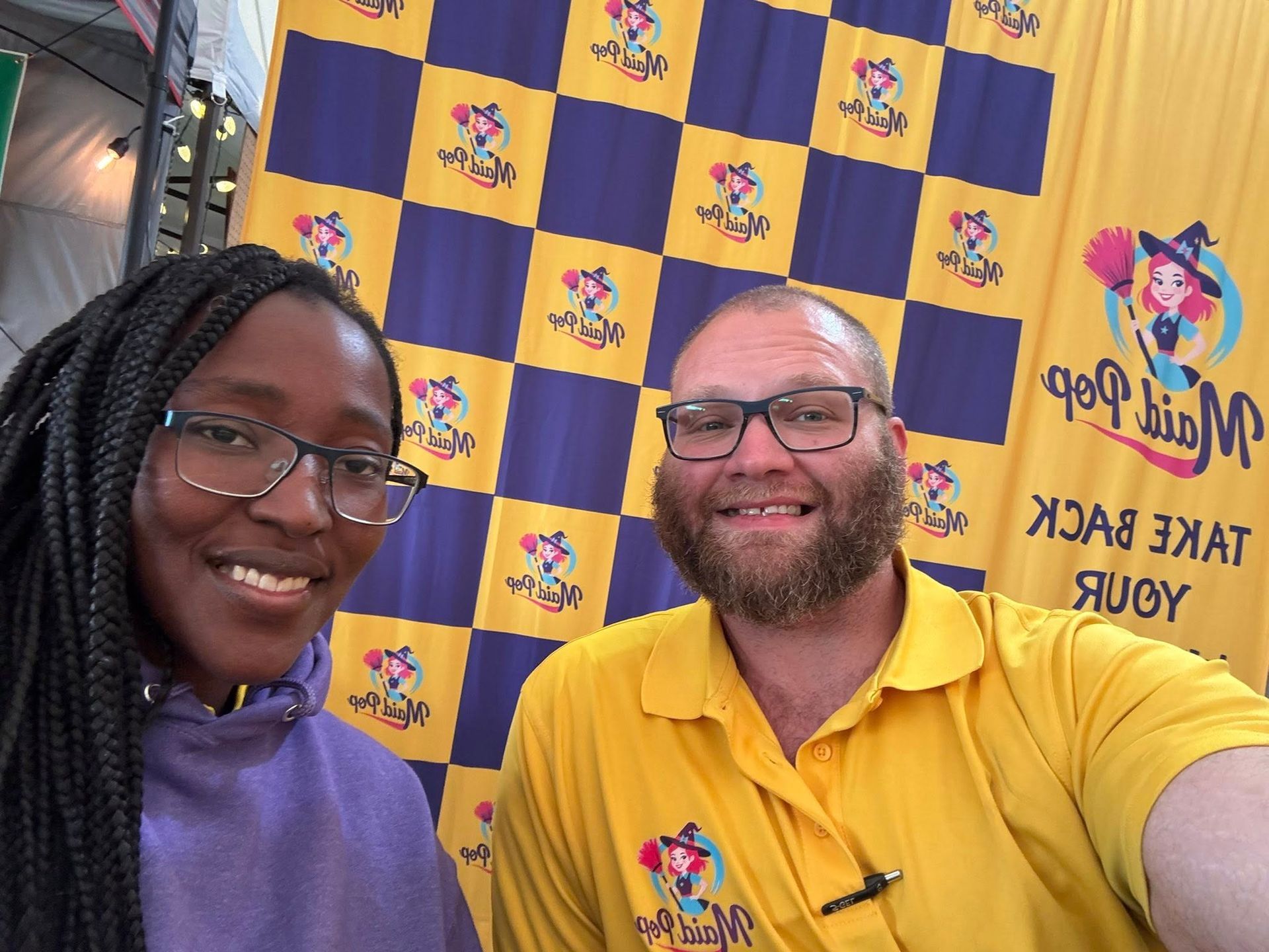 Two people smile in front of a checkered yellow/purple backdrop