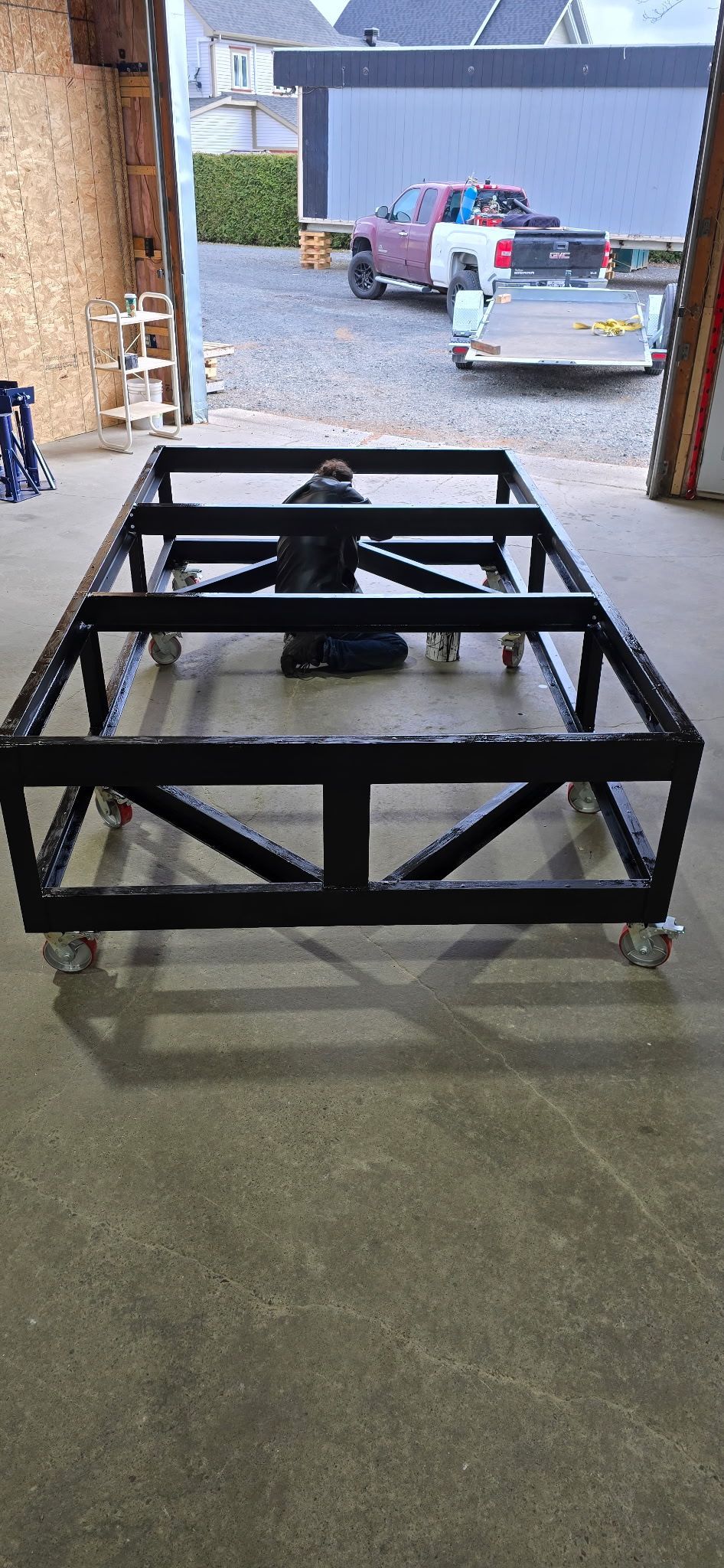 Un cadre métallique noir sur roues à l'intérieur d'un garage. Des camions et des bâtiments sont visibles en arrière-plan.