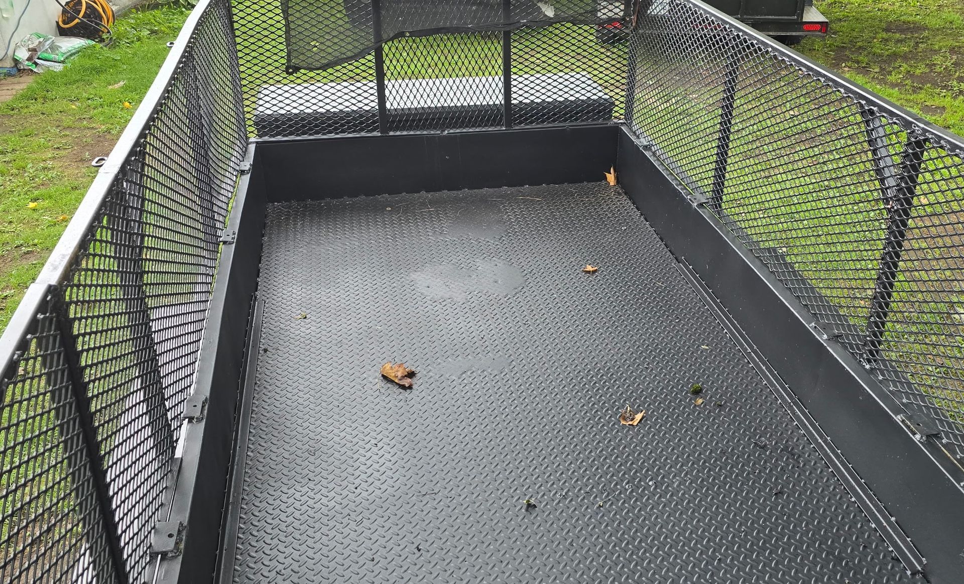 Remorque utilitaire noire avec côtés grillagés, vide, à l'extérieur sur l'herbe verte.