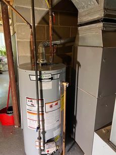 A water heater is sitting next to a furnace in a basement.