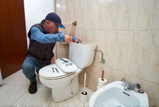 A man is fixing a toilet in a bathroom.