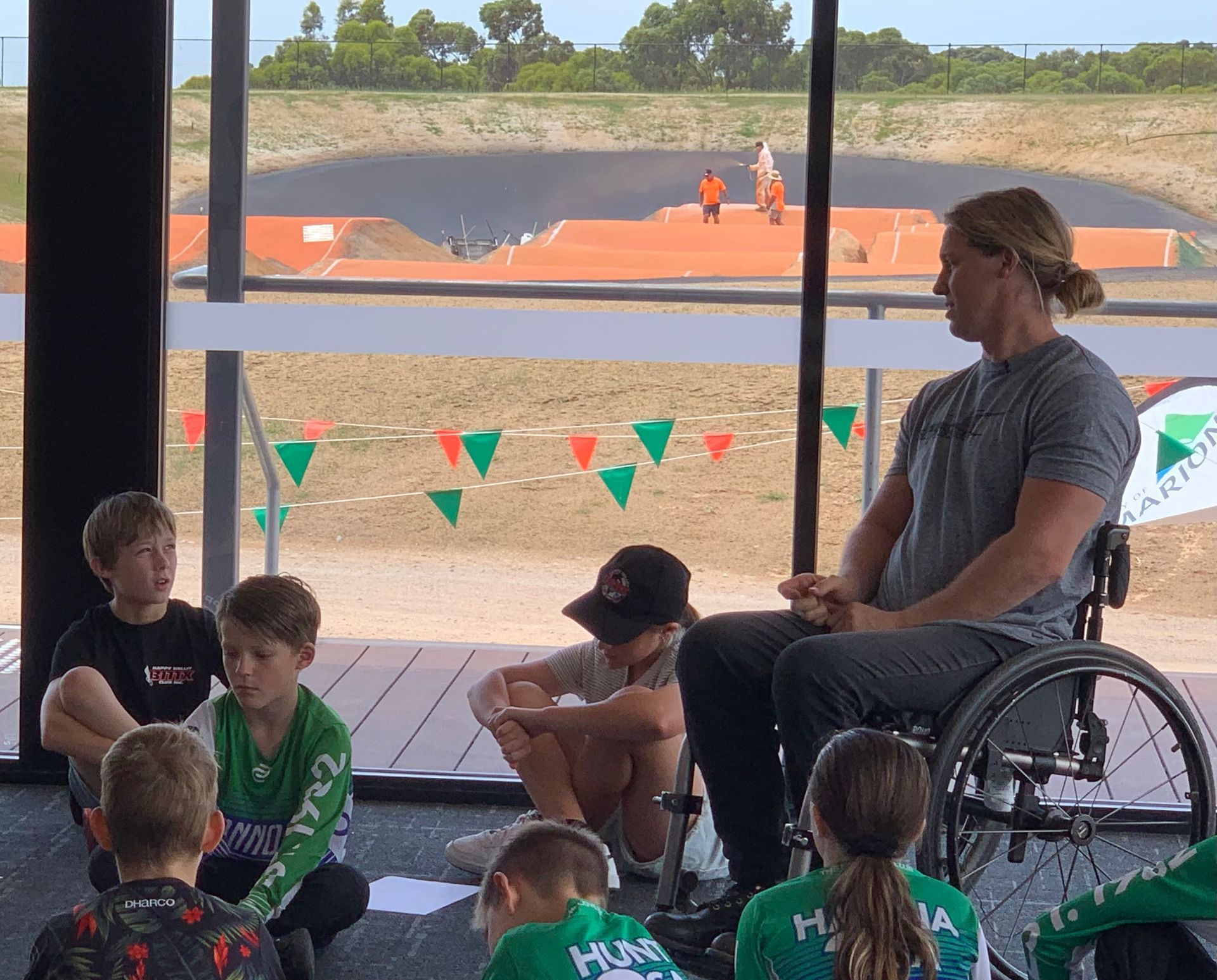 A man in a wheelchair is talking to a group of children.