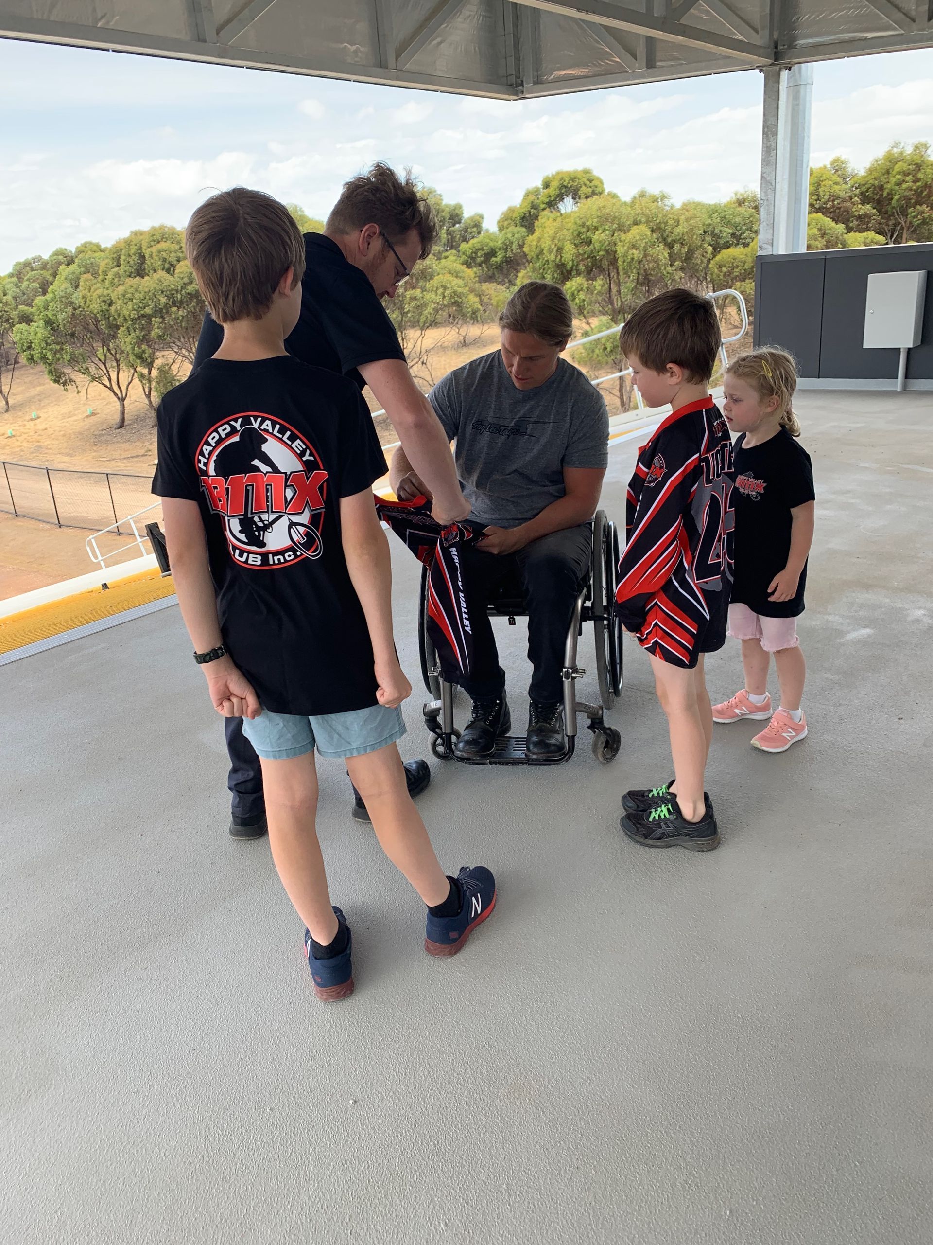 A group of children are standing around a man in a wheelchair.