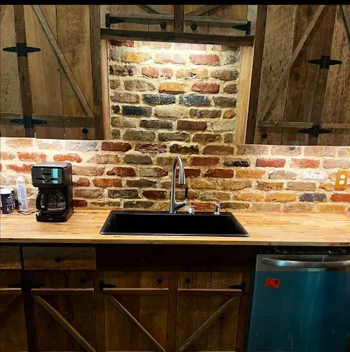 Kitchen with brick backsplash, wooden cabinets and countertop, black sink, and stainless steel appliances.