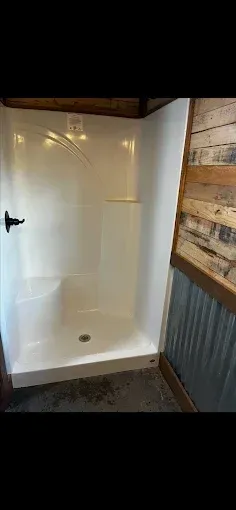 White shower stall with black handle in a room with corrugated metal and wood siding.