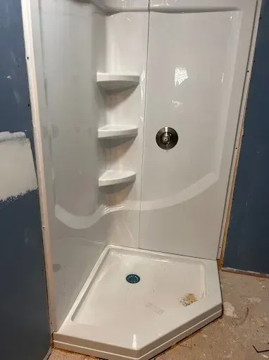 White corner shower stall with built-in shelves and a chrome fixture, in a room with blue walls.