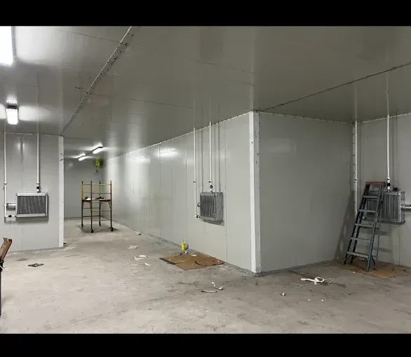White-walled interior space. Refrigeration units, ladder, shelving, and a concrete floor.