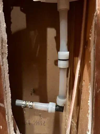 White and black plumbing pipes in a wall cavity; two connections, one with a clamp.