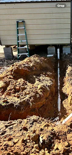 A trench with white PVC pipes leading to a building. A ladder leans against the building.