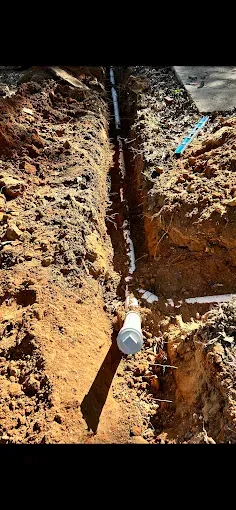 Trench dug in brown earth with white and black piping running through it.