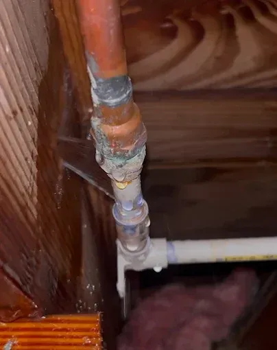 Copper pipe joint with significant corrosion and water leak in a wood-framed ceiling.
