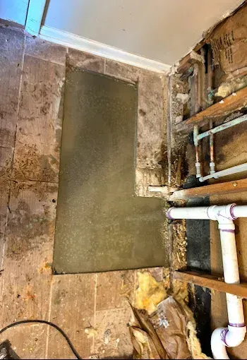 Bathroom wall under construction; exposed plumbing, cement patch in wall, brown tile.