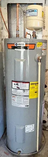 A tall gray water heater in a room, with copper pipes and a white expansion tank.