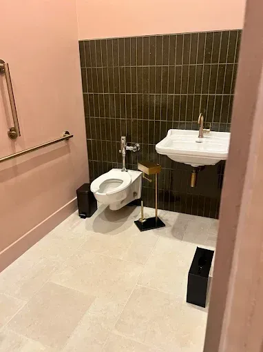 A small, pink-walled restroom with a toilet, sink, gold fixtures, and dark green tiled wall.