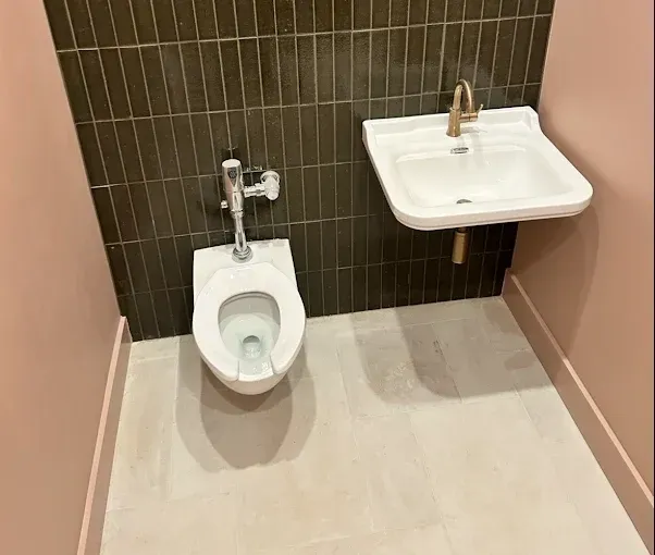 Small accessible restroom with toilet, sink, dark tile accent wall, pink walls, and light tile floor.