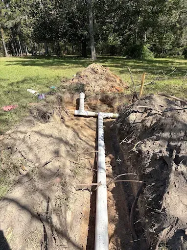 White PVC pipes in a trench, part of an outdoor plumbing project in a grassy area.