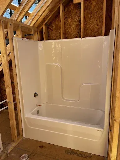 White bathtub/shower unit installed within the wooden framing of a construction project.