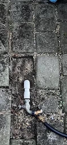 Outdoor water spigot on a brick patio with a connected black hose.