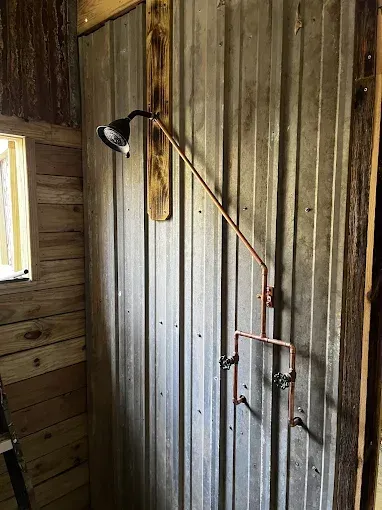Copper shower fixture against corrugated metal wall in rustic wooden shower.