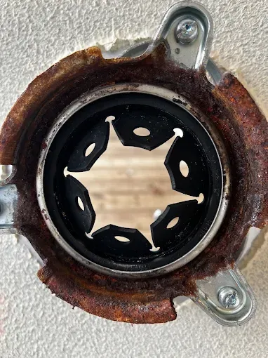 Rust-covered garbage disposal flange with a black rubber seal, inside a hole in a wall.