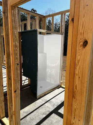 Framed wooden construction surrounding a white shower stall with a dark green exterior panel.