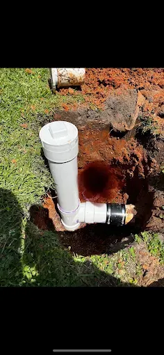 PVC pipe installed in a hole in the ground, surrounded by grass and dirt.