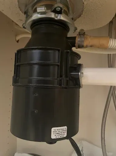 Black garbage disposal unit installed under a white kitchen sink, connected to plumbing.