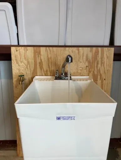 White utility sink with running water, mounted on plywood backing.