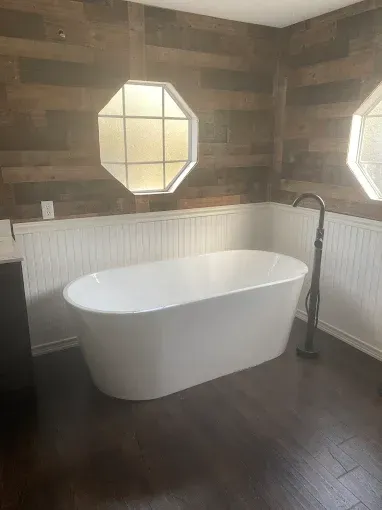 Freestanding white bathtub in a bathroom with wood-paneled walls, a dark floor, and octagonal windows.