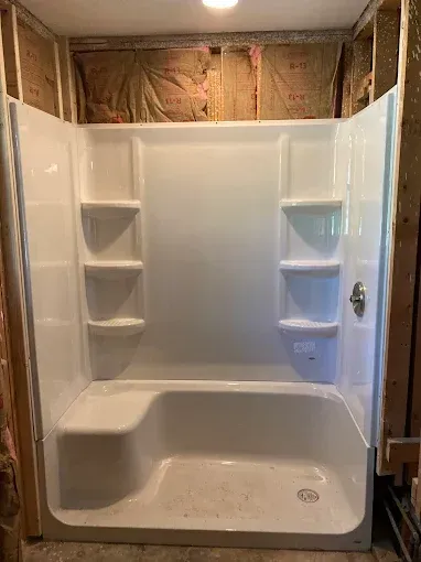 White alcove shower unit installed in a room under construction, with shelves on both sides, and a built-in seat.