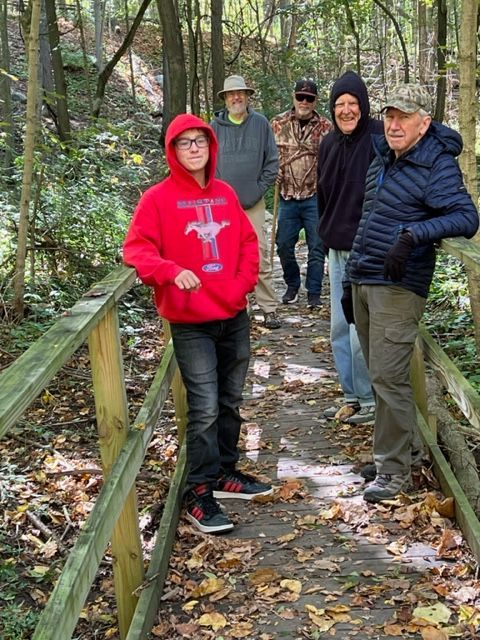 a group of people are standing on a wooden bridge in the woods .