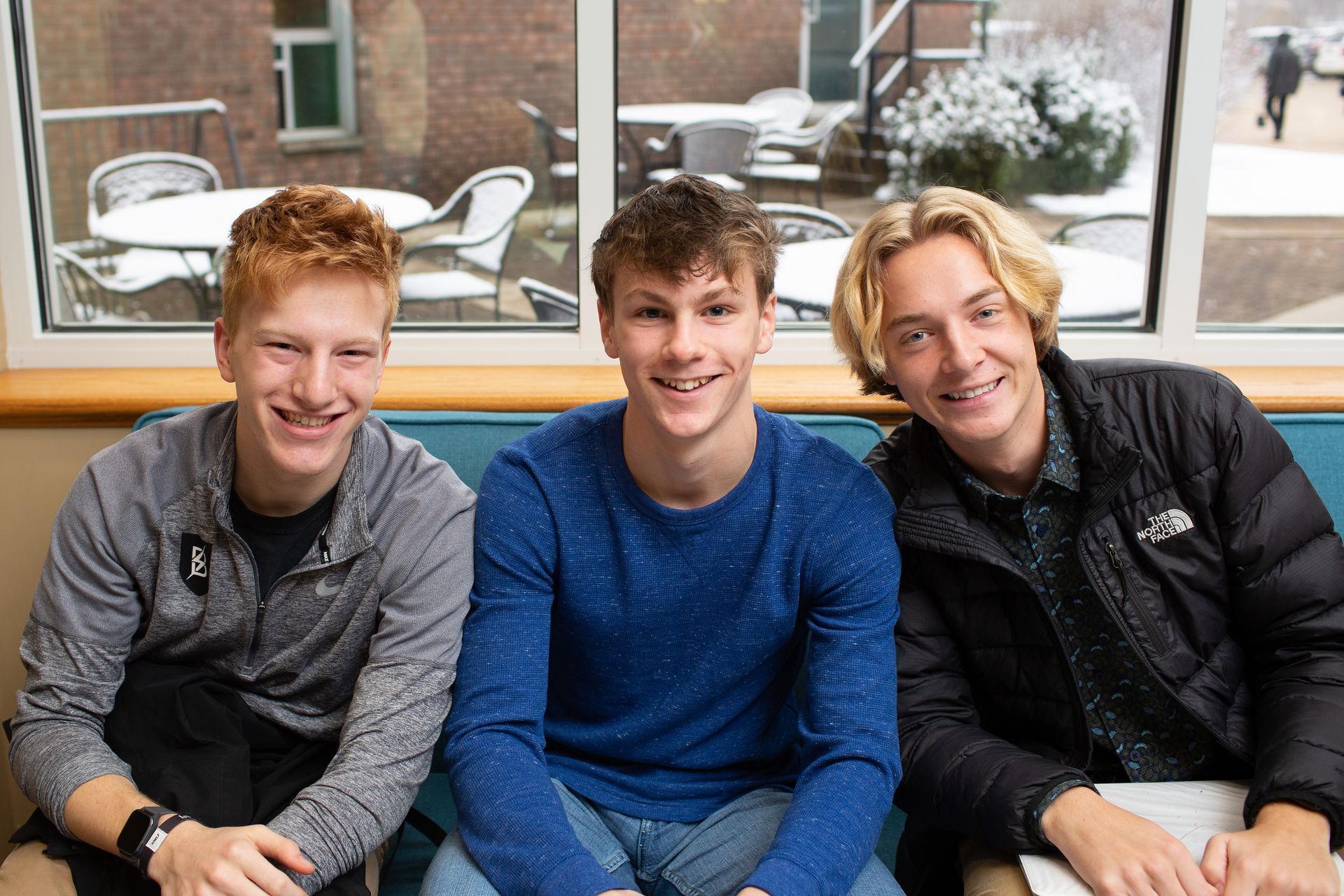 three young men are sitting next to each other in front of a window .