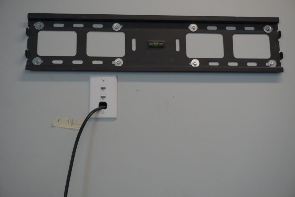 A tv mount is attached to a wall with a cord plugged into it.