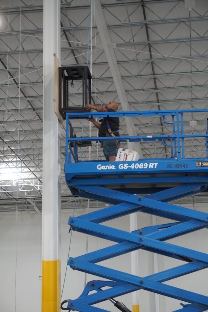 A man is working on a blue scissor lift in a warehouse.