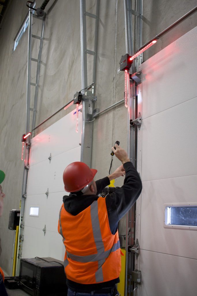 A man in an orange vest and hard hat is working on a garage door.