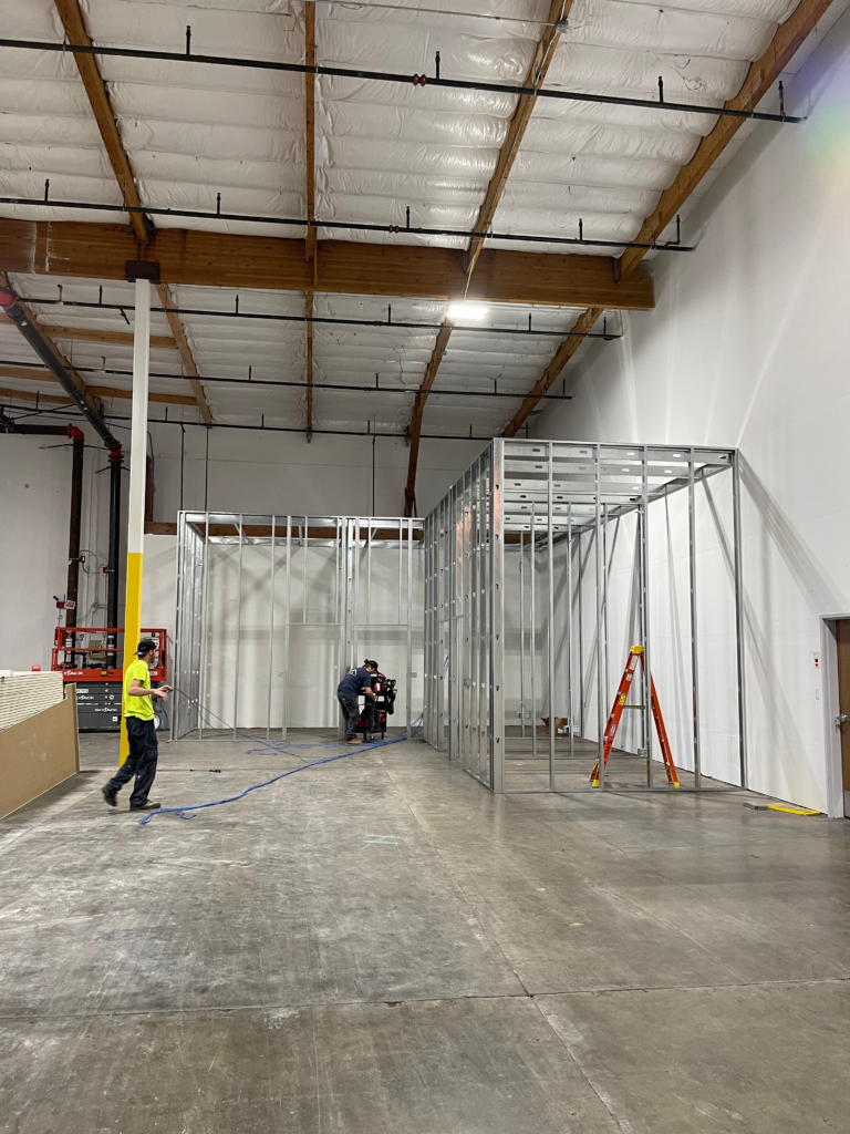 A man in a yellow vest is standing in a large warehouse.