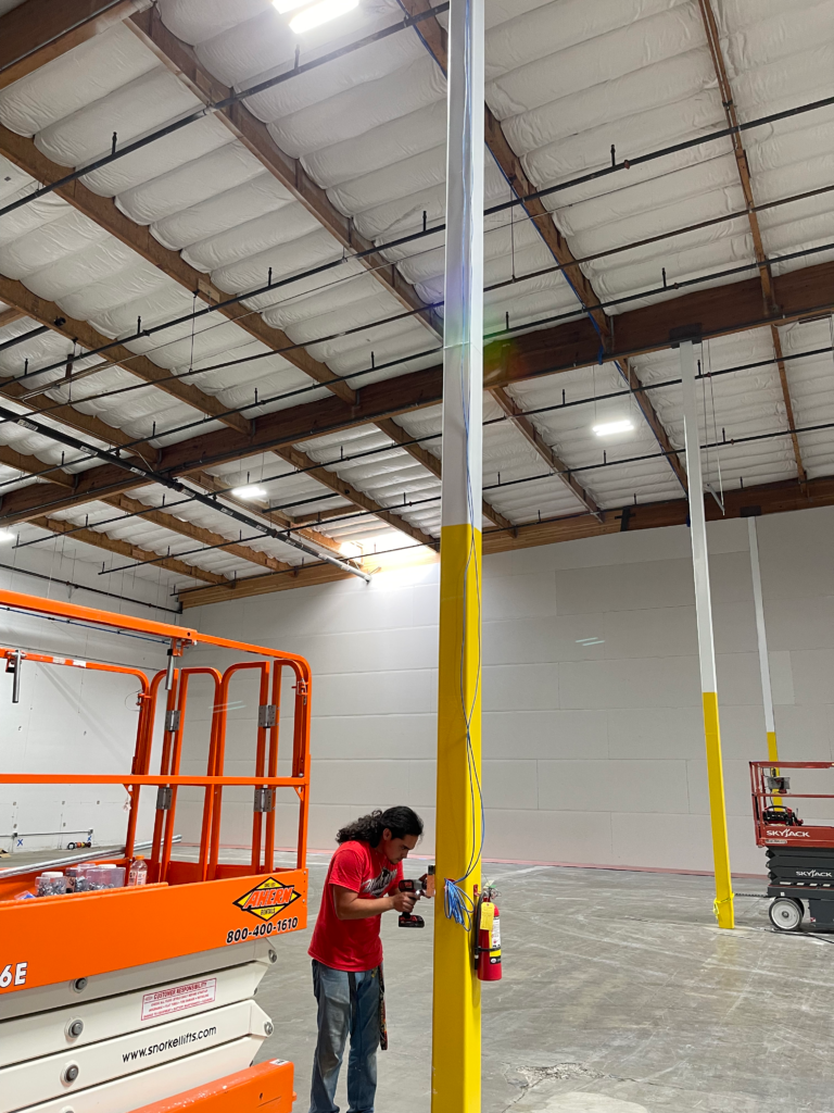 A man is standing next to a yellow pole in a large warehouse.