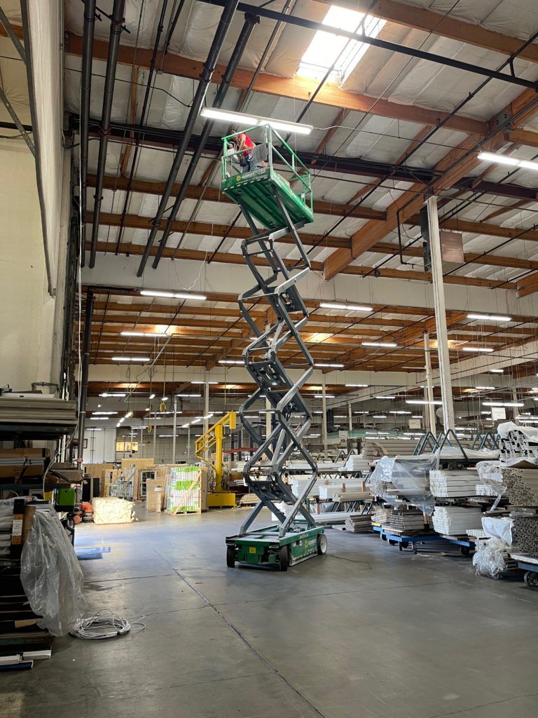 A man is standing on a scissor lift in a large warehouse.