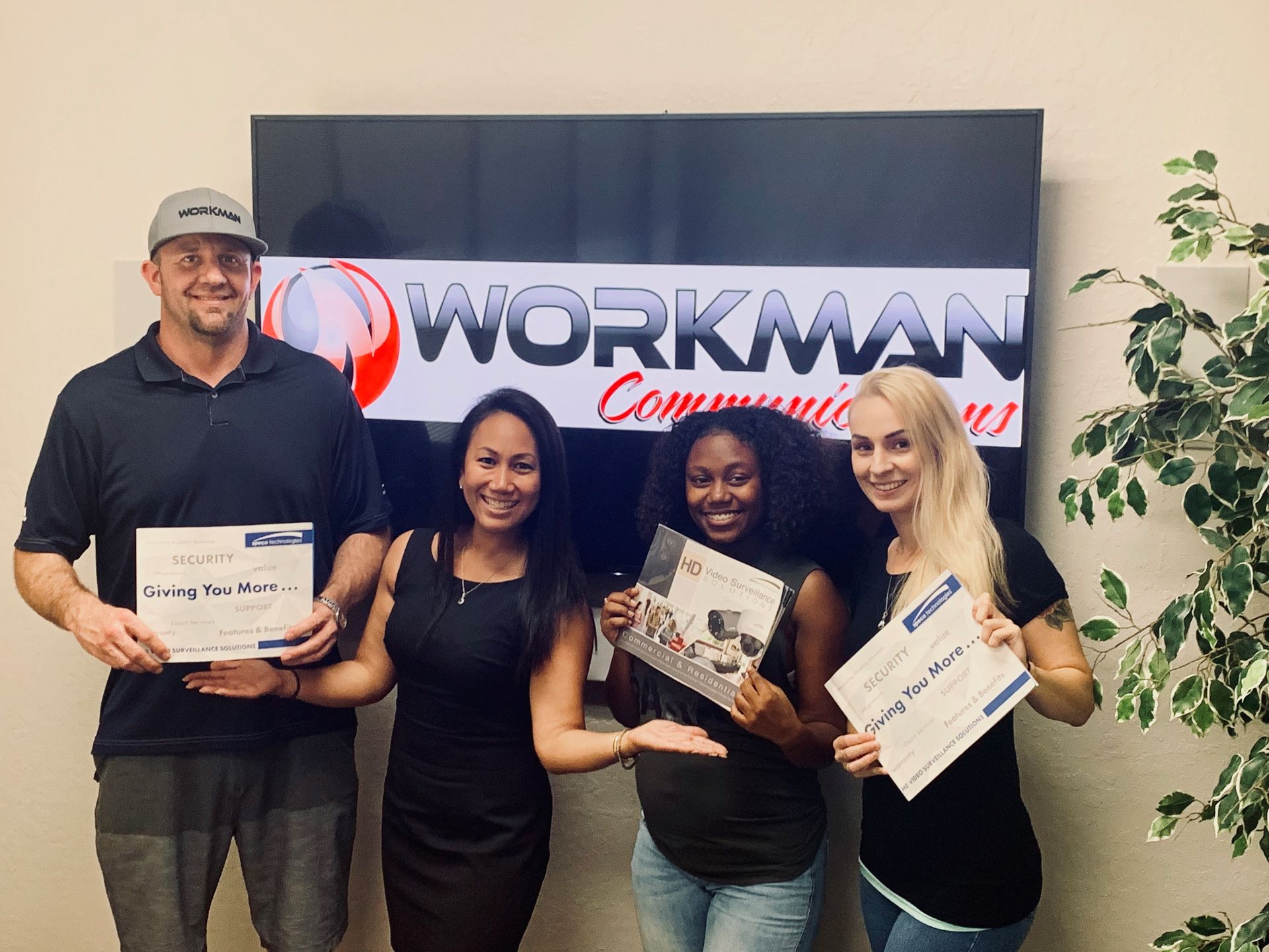 A group of people are posing for a picture in front of a workman communications sign.