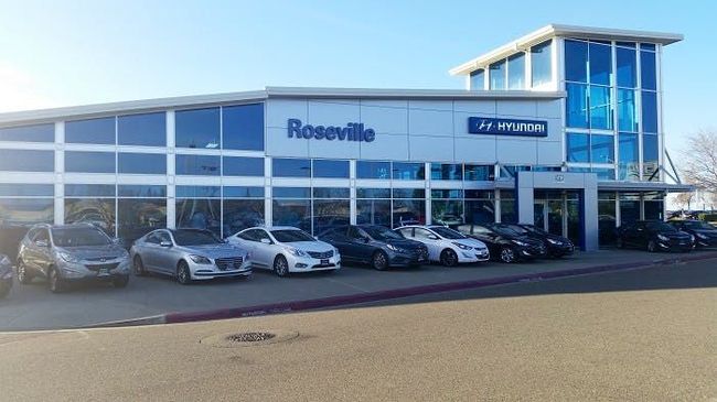 A row of cars are parked in front of a car dealership.