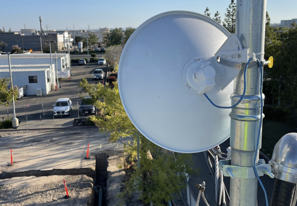 A white satellite dish is sitting on top of a metal pole.