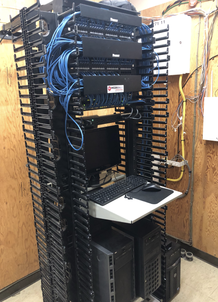 A server rack with a laptop on a shelf in a room.