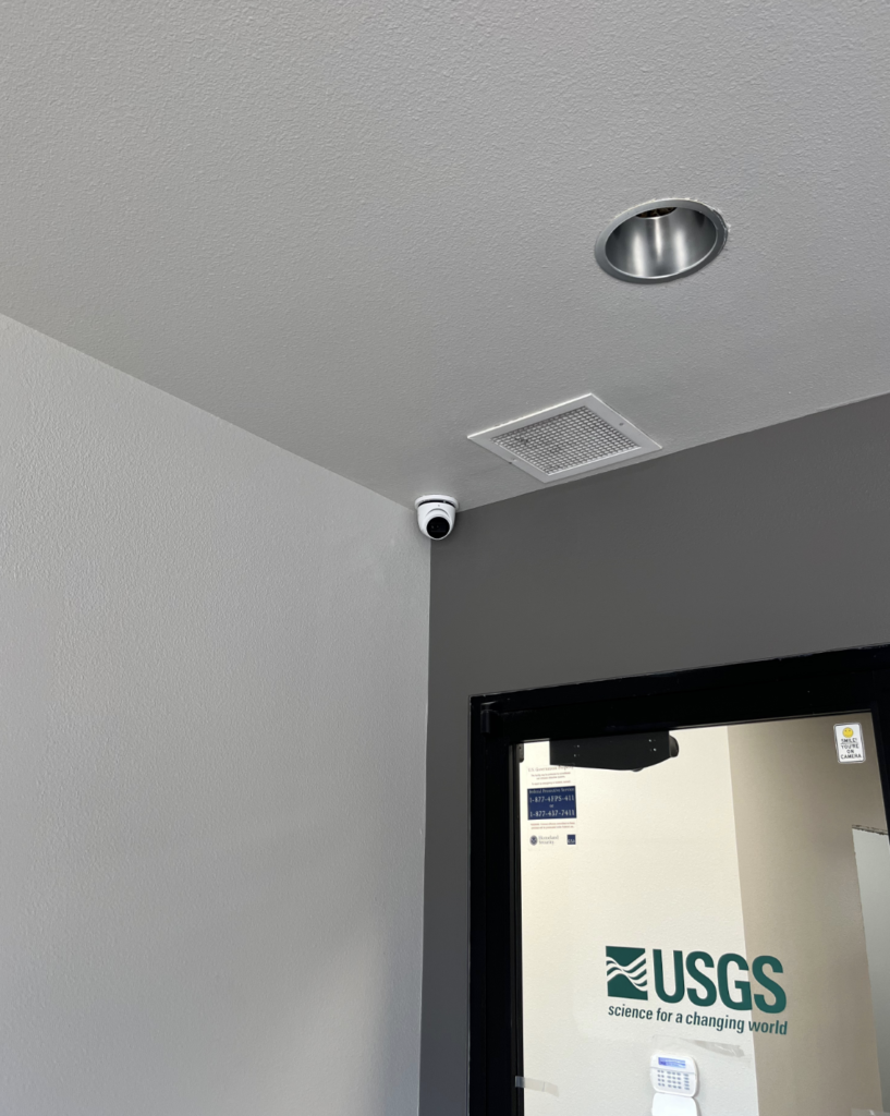 A camera is mounted on the ceiling of a room next to a door.