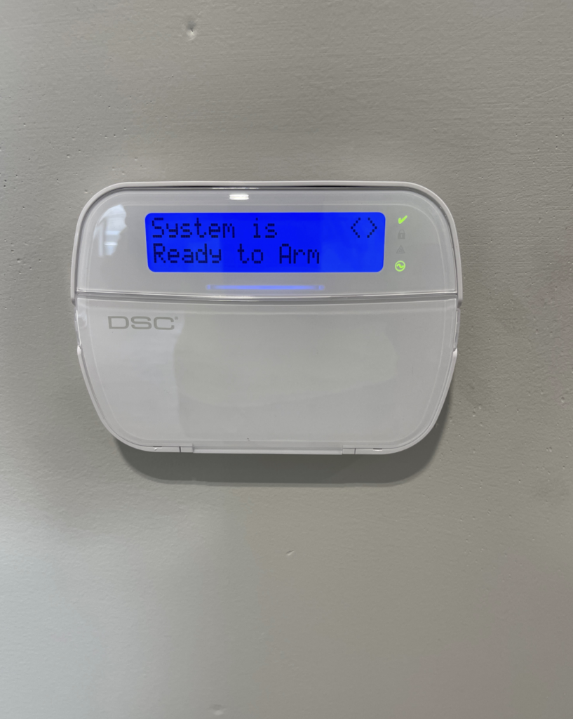 A white alarm system is hanging on a wall.