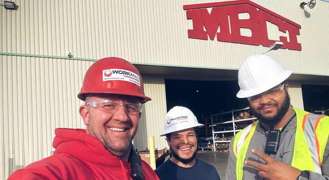 Three men wearing hard hats and safety vests are standing in front of a building.