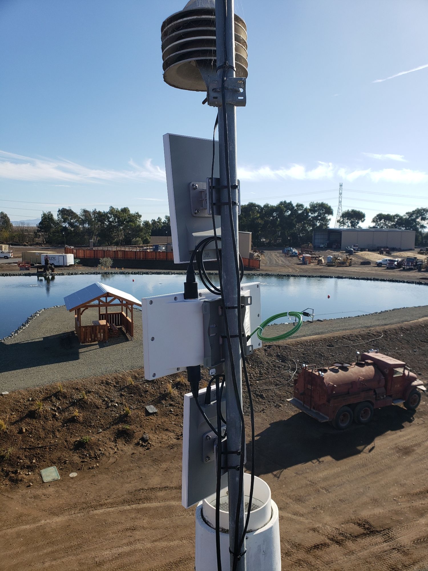 A weather station is sitting on top of a pole next to a body of water.