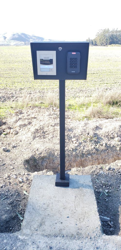 A black mailbox is sitting on top of a concrete post in a field.