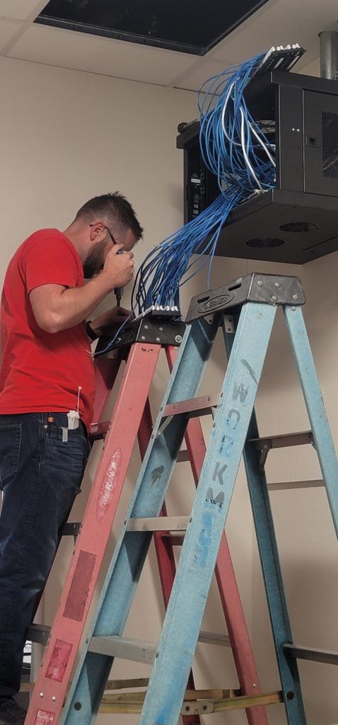 A man is standing on a ladder working on a computer.